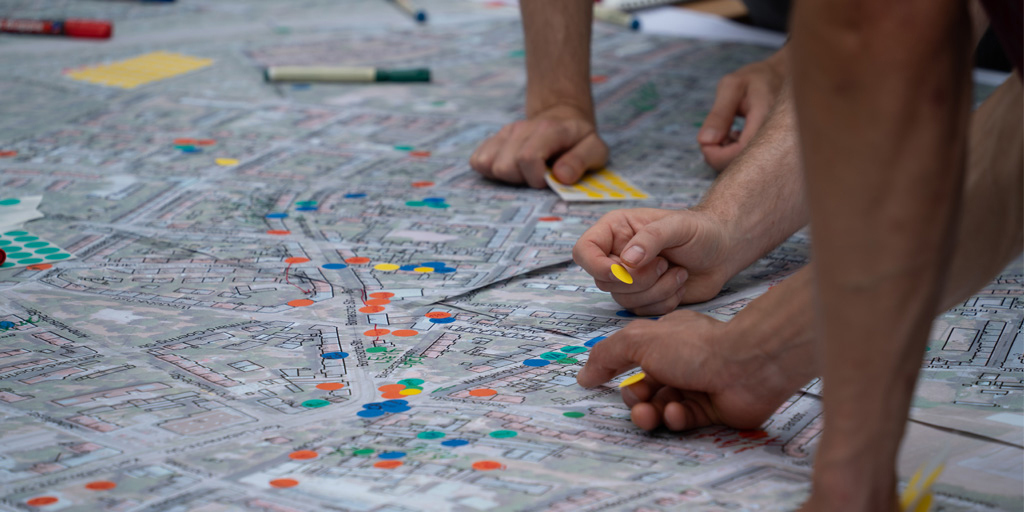 gezeichneter Stadtplan mit bunten Klebepunkten und Händen, die auf dem Plan arbeiten